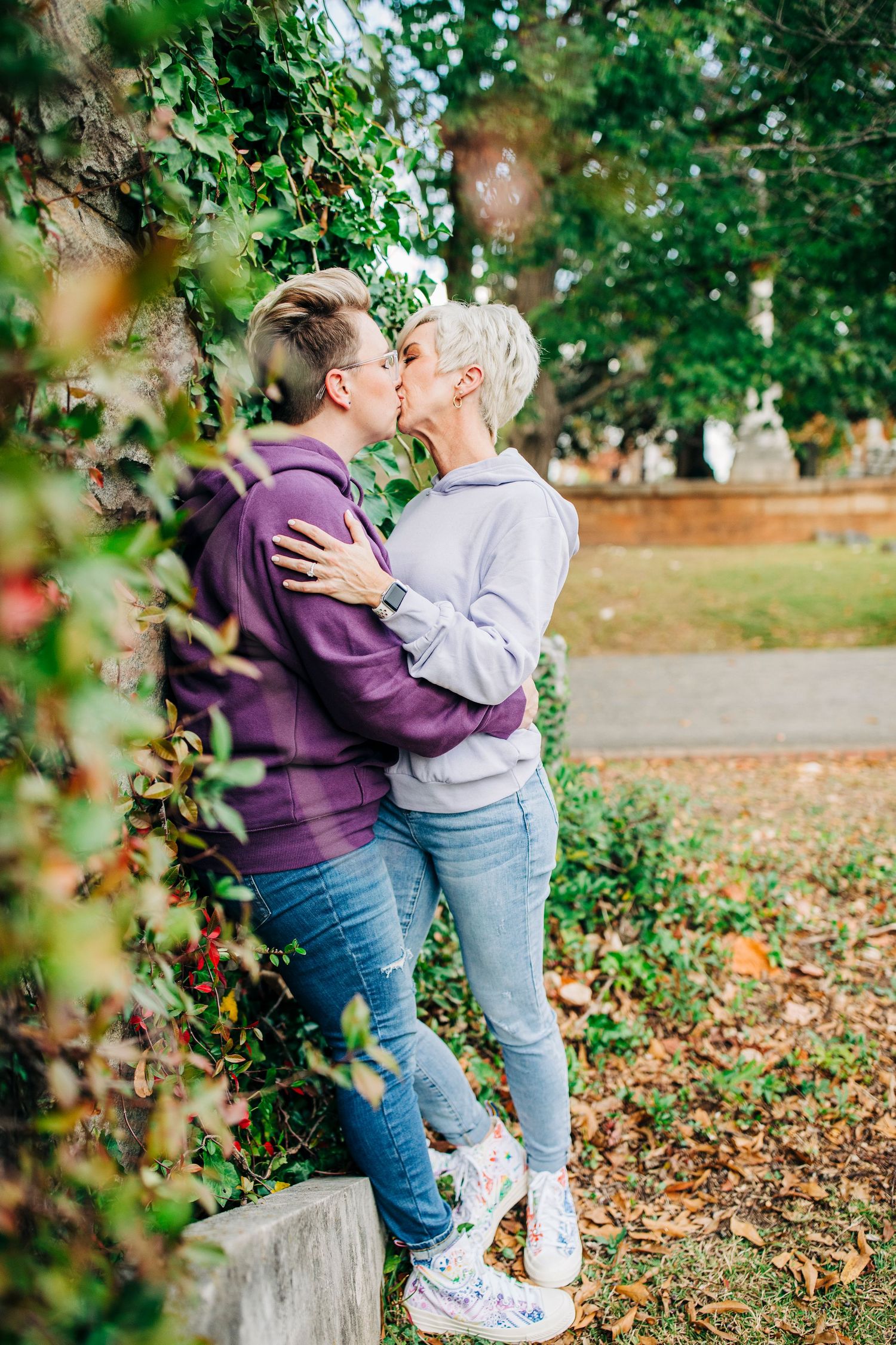 Couple sharing an intimate moment among fall foliage while wearing purple and grey hoodies.