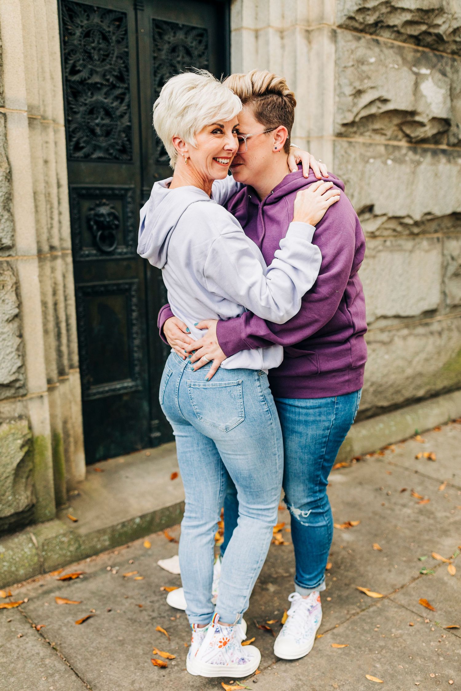 Couple sharing a playful moment against a stone wall with ornate door in background.
