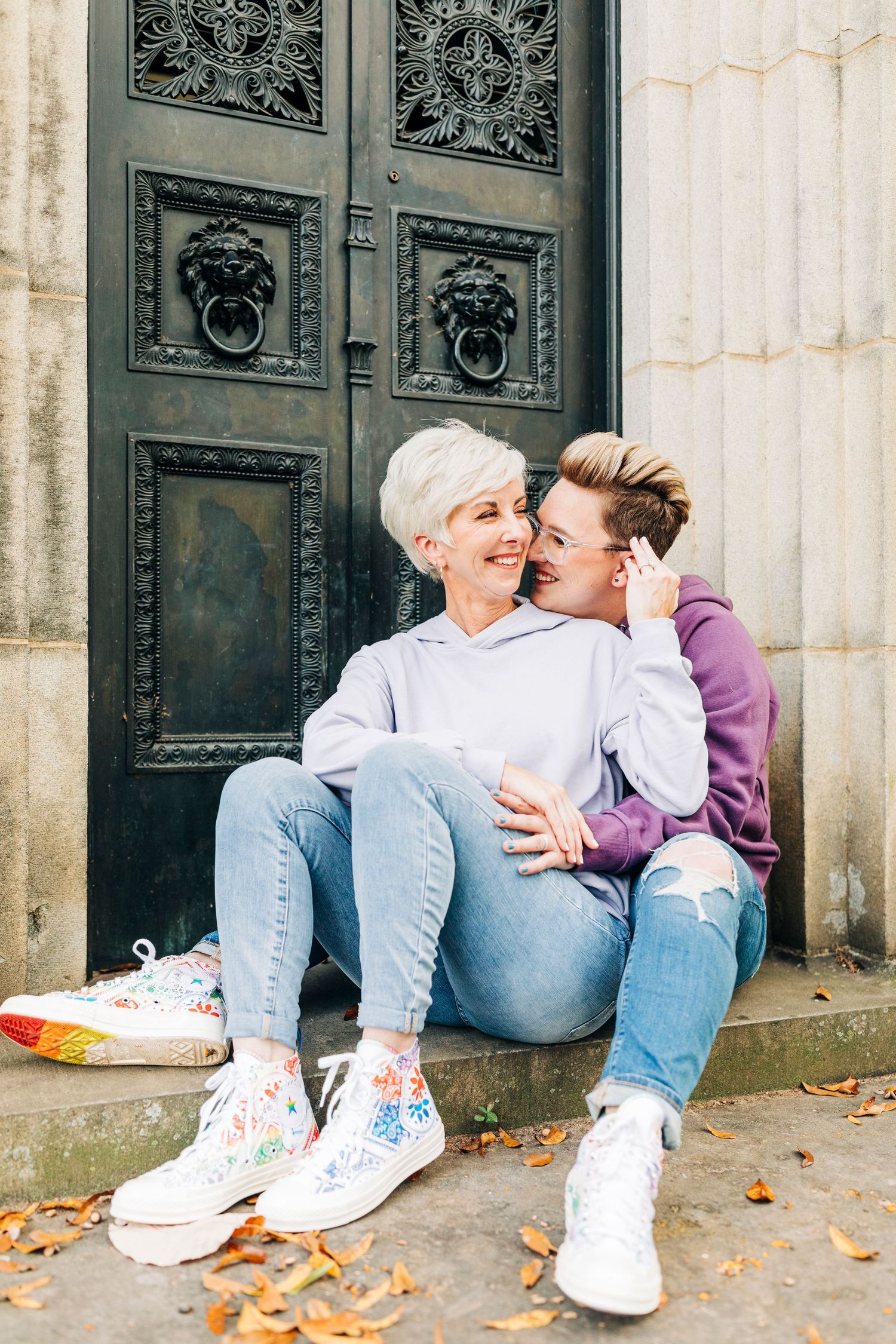 Two people in casual clothes sitting and laughing together by an ornate vintage door.