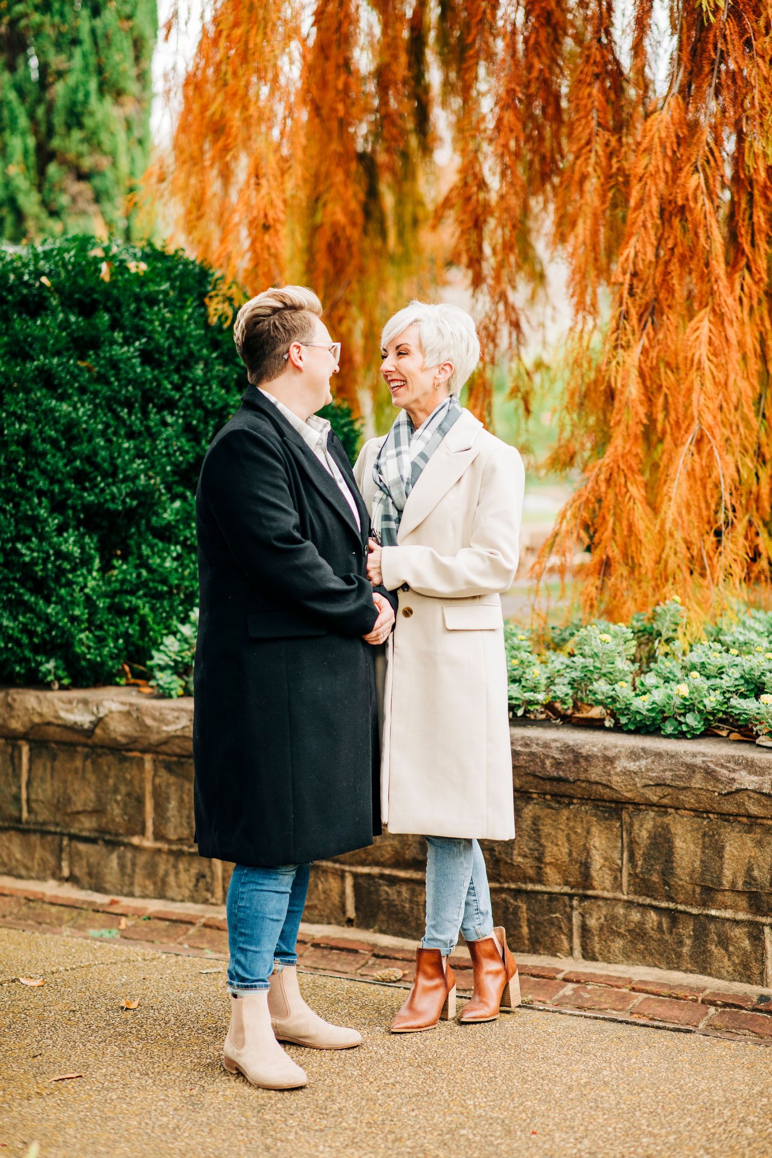 Couple in winter coats sharing intimate moment against backdrop of orange autumn tree.