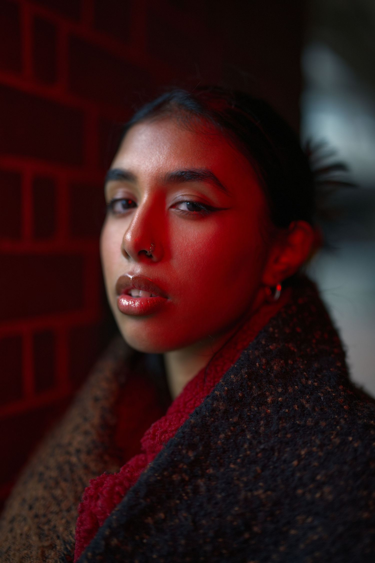 Dramatic red-lit portrait against brick wall with moody lighting and warm tones.