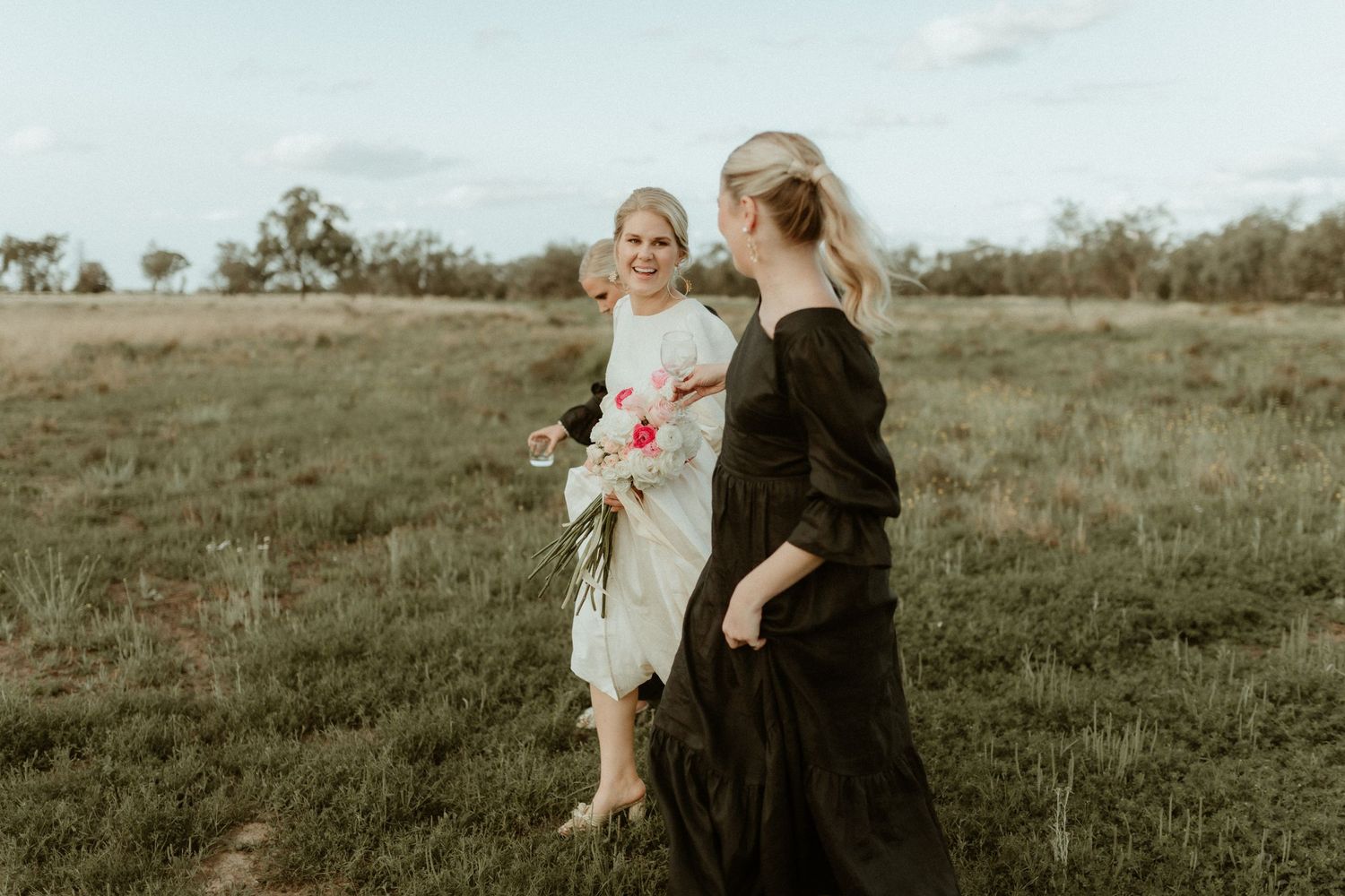 Two women in contrasting dresses walk together through a grassy field.