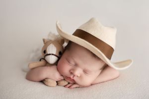 Sleeping newborn boy with tiny cowboy hat and cuddling a horse stuffed animal
