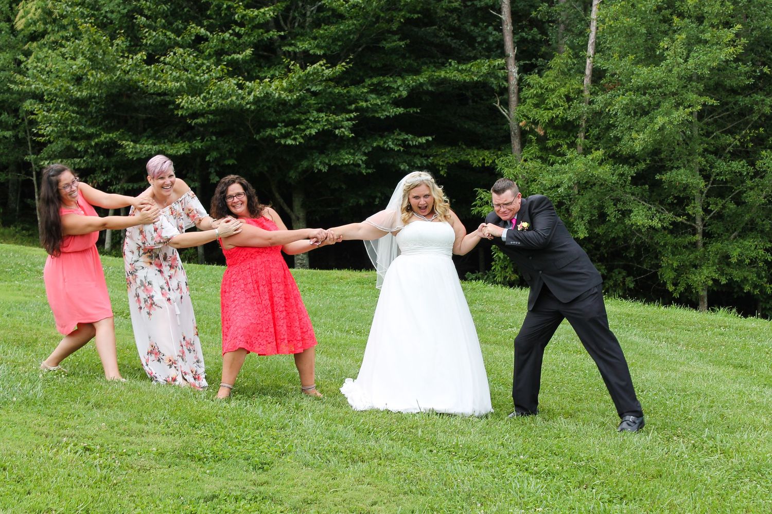 Playful wedding party pose making wave formation on grassy hillside.