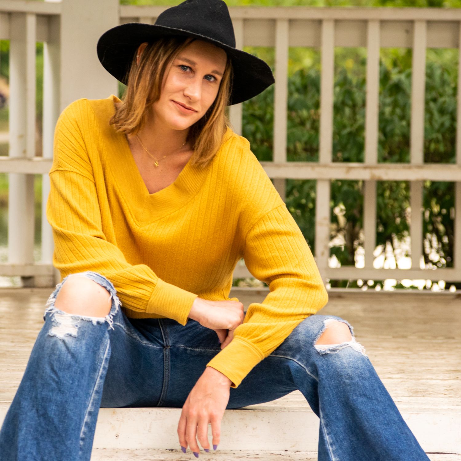 Headshot Portrait Session. A young adult woman sits on the steps of a gazebo in a gold sweater with a black boho hat.