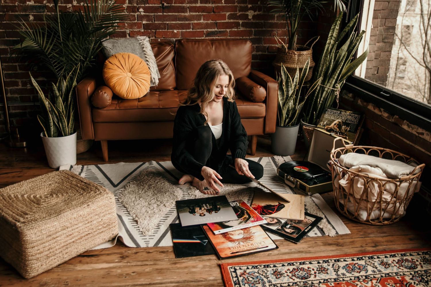 Person looking through photo albums on a brown leather couch with indoor plants and autumn decor.
