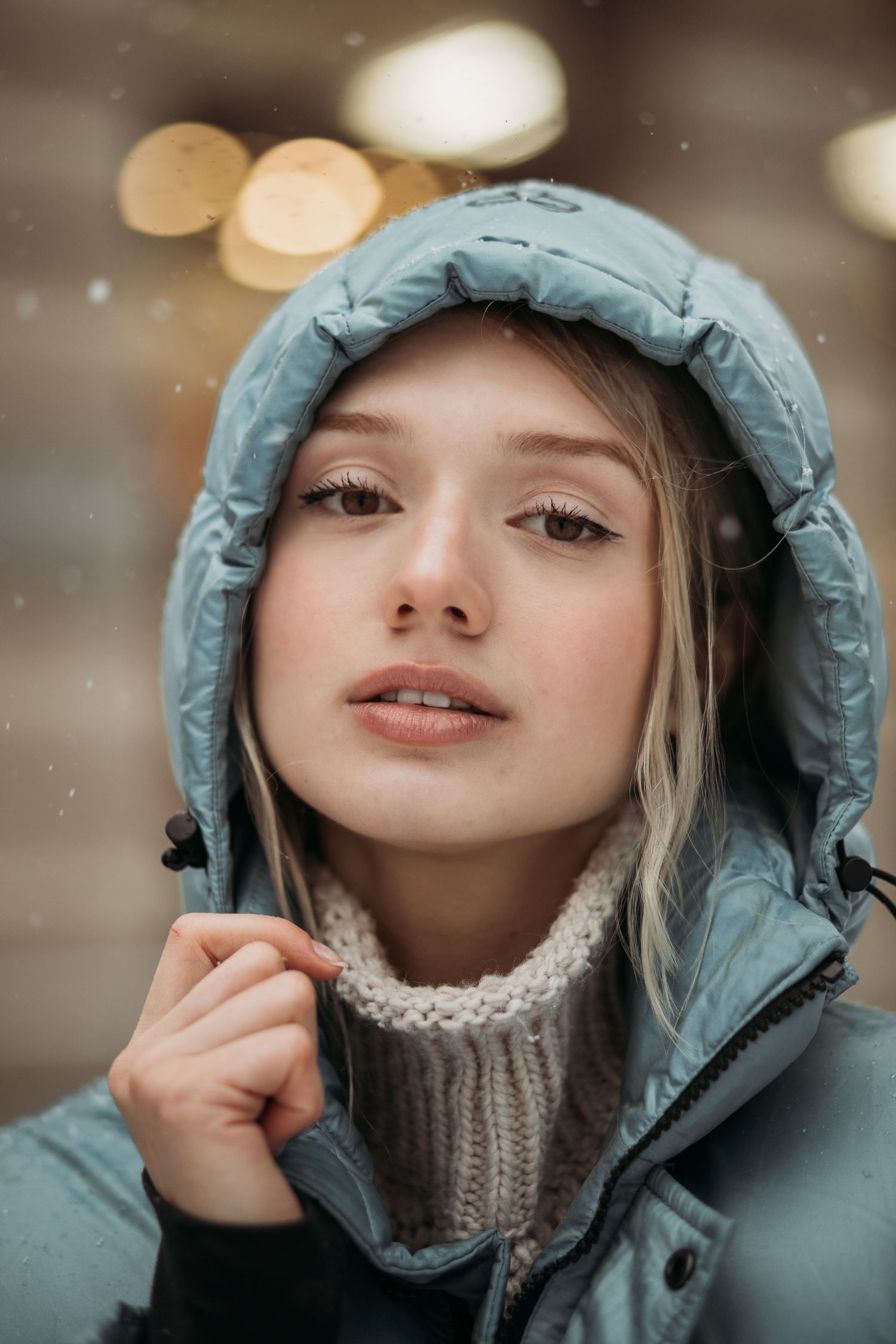 Close-up portrait of someone wearing teal winter coat with hood and cream turtleneck.