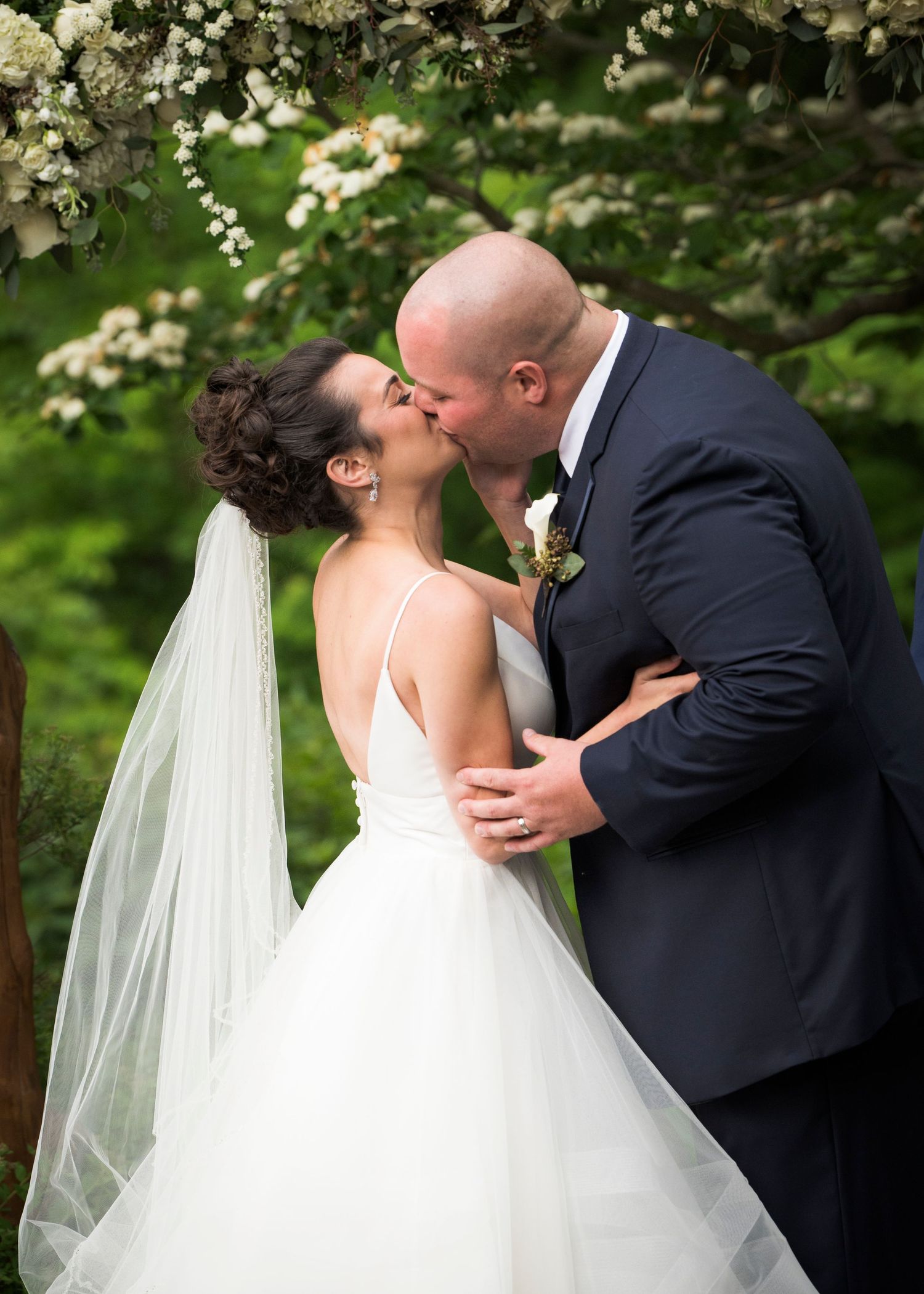 A romantic wedding kiss under blooming white flowers during a spring ceremony.