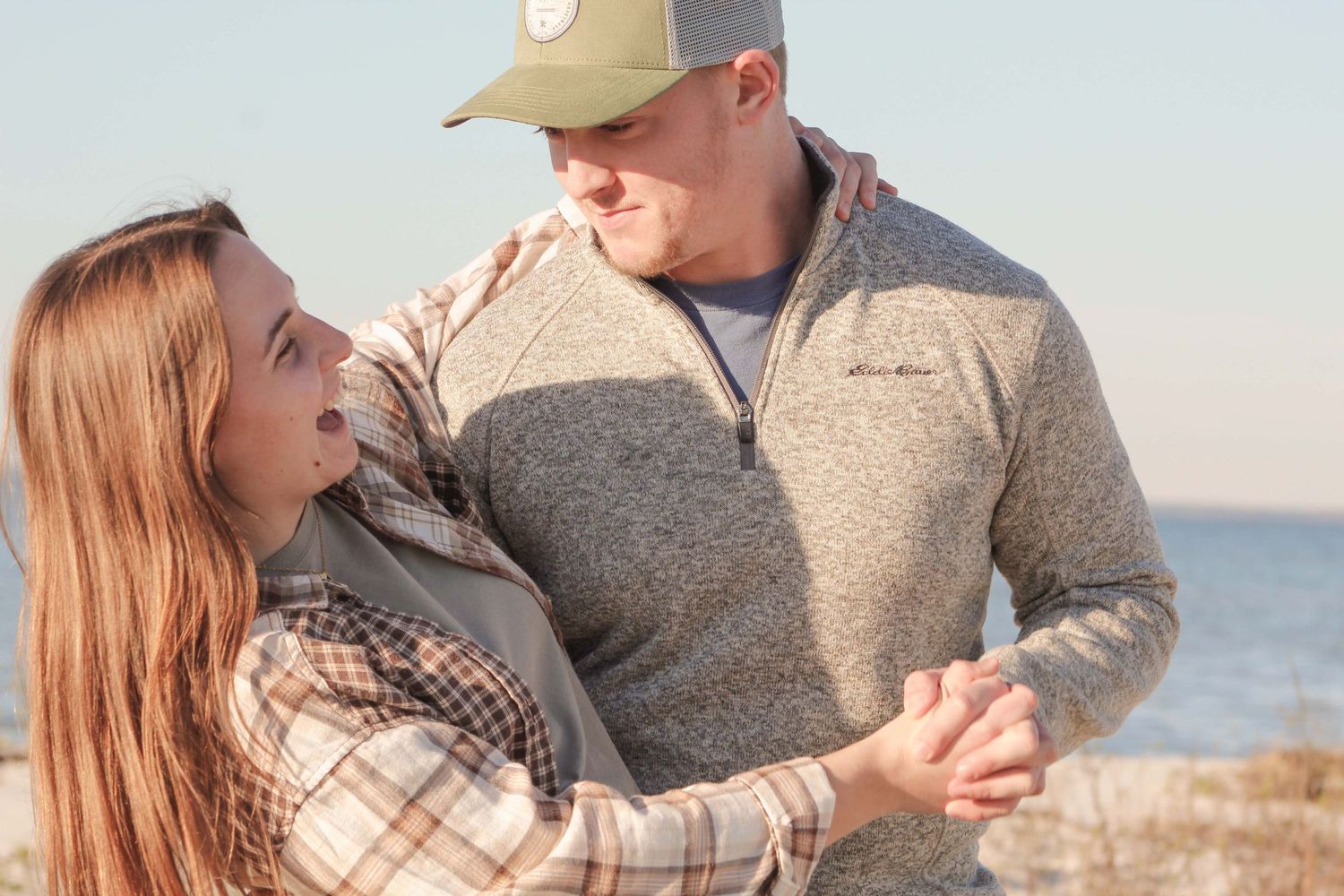 Couple in casual attire shares tender moments on a beach at sunset.