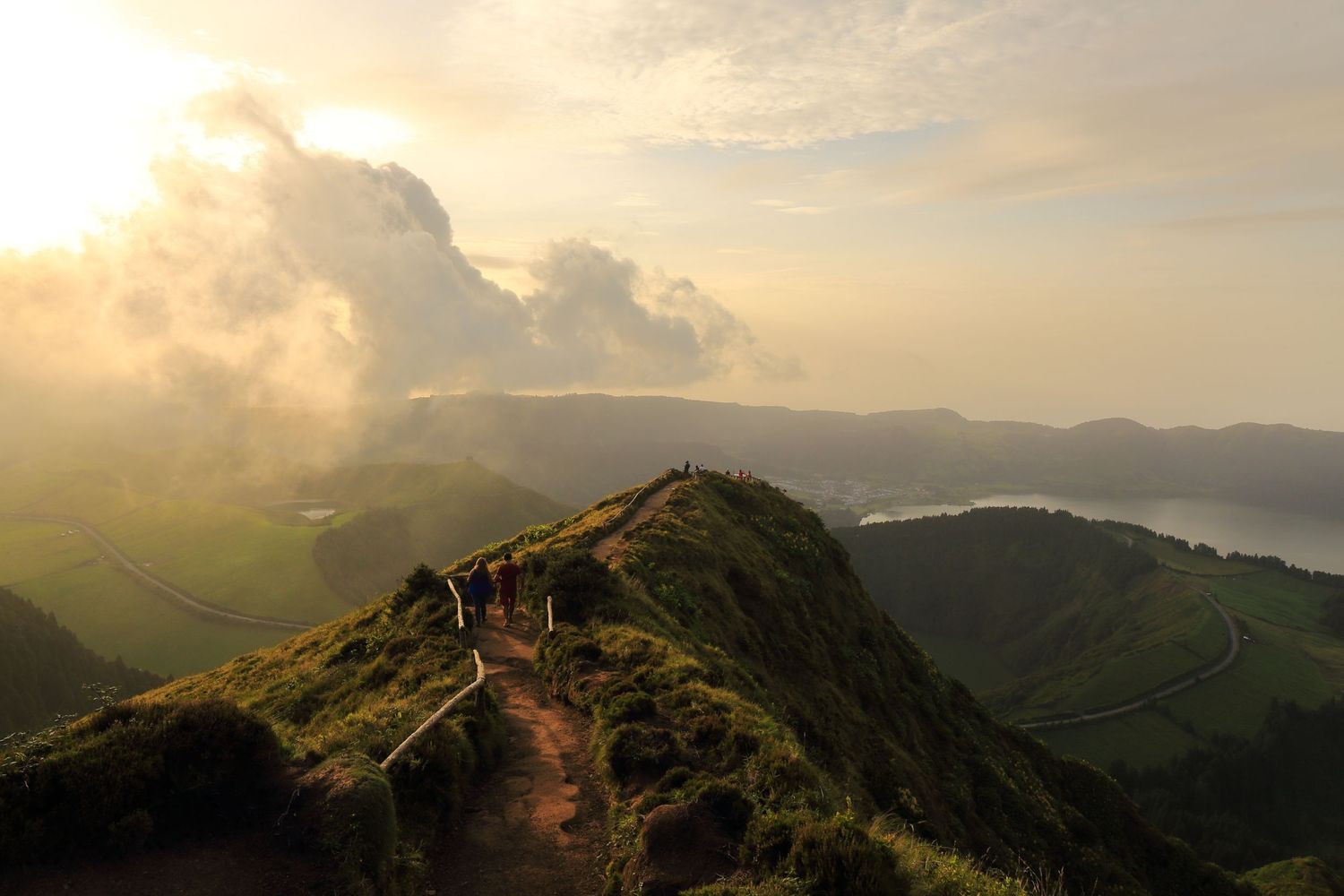 Hiking trail along a dramatic mountain ridge with golden sunset light and clouds in the background.
