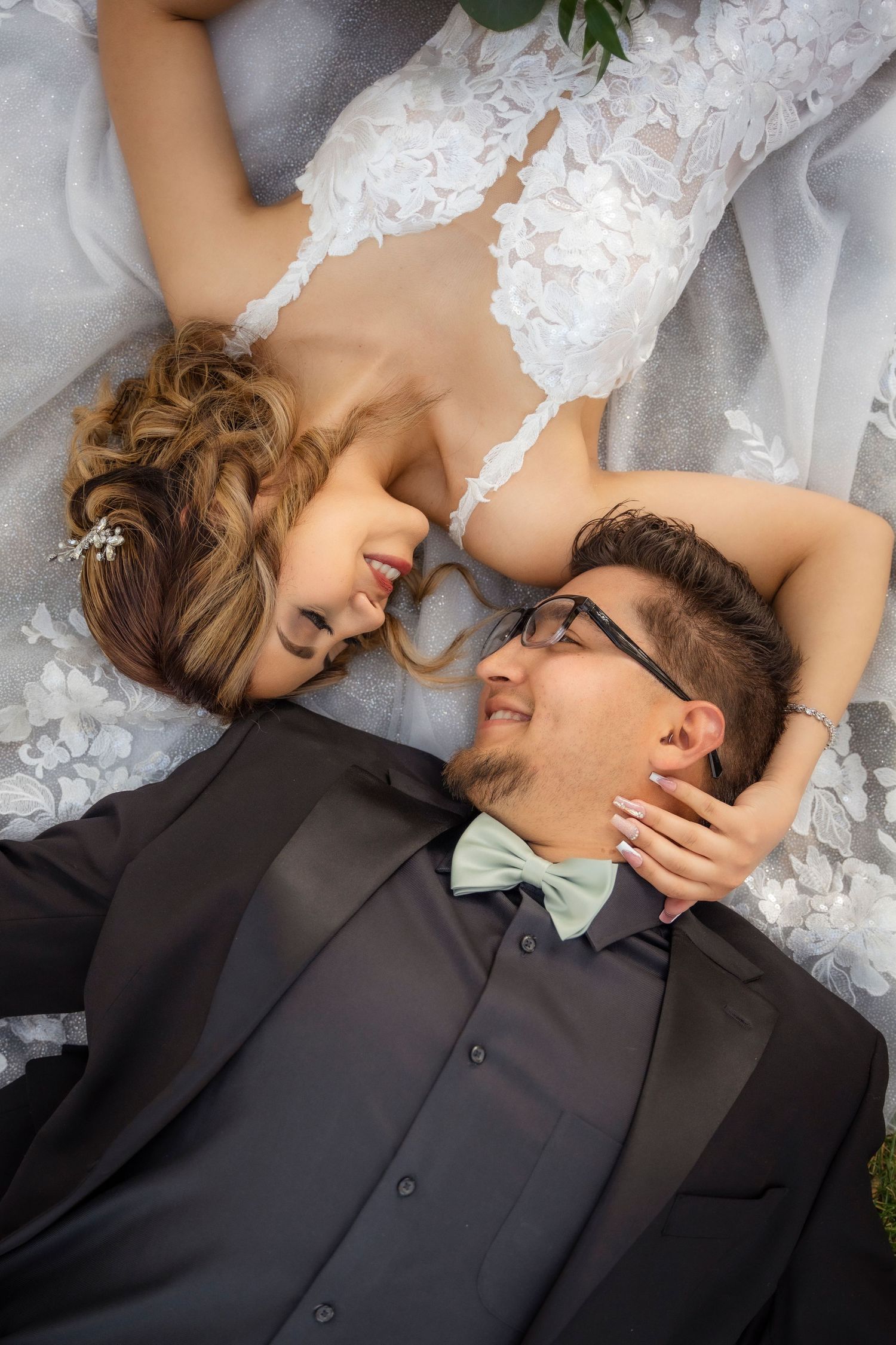 Bride and groom lying down gazing at each other, groom in black tuxedo with mint bow tie.