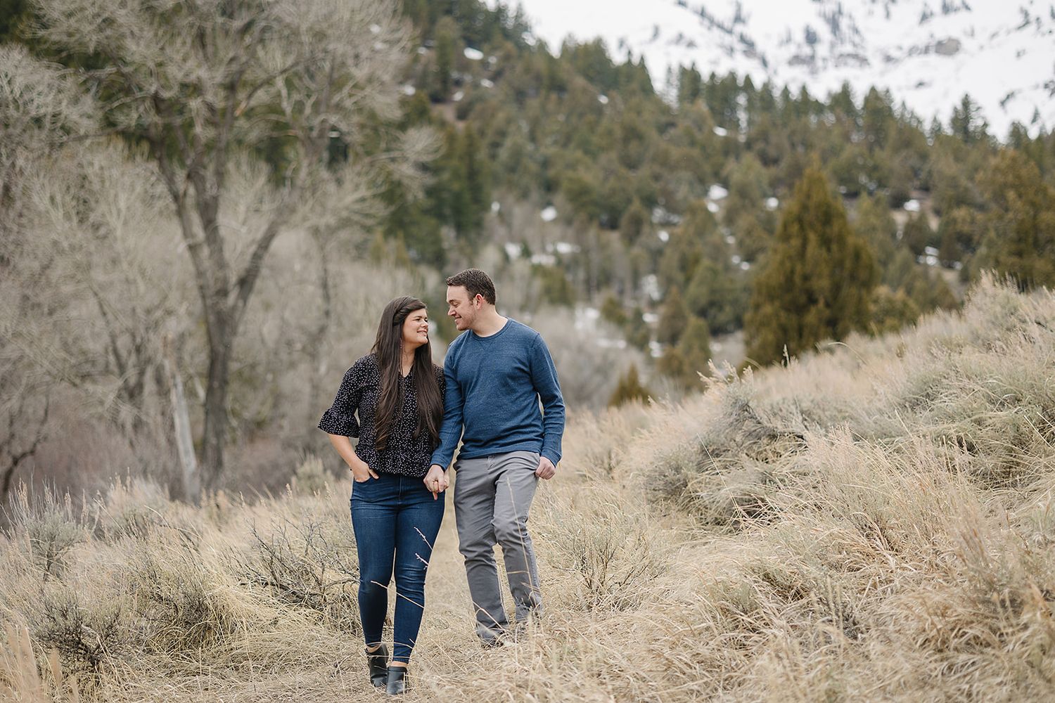Casual couple walking together on a hillside trail with mountain scenery behind them.