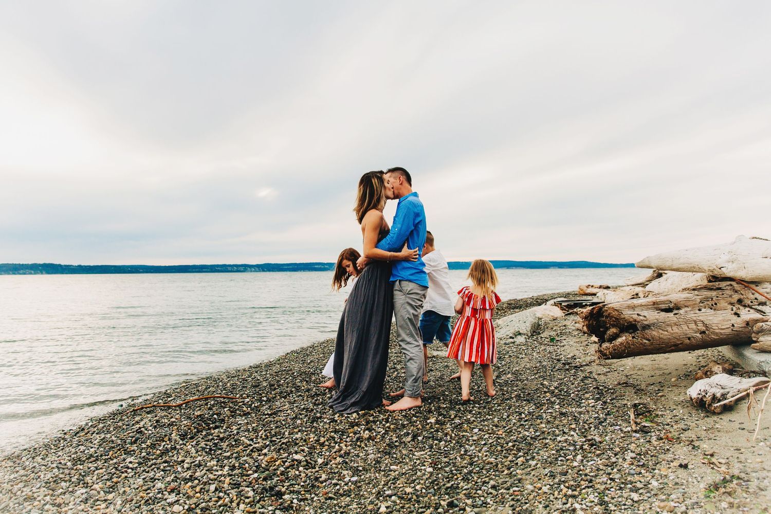 Candid shot of parents kissing with kids circling them on the beach