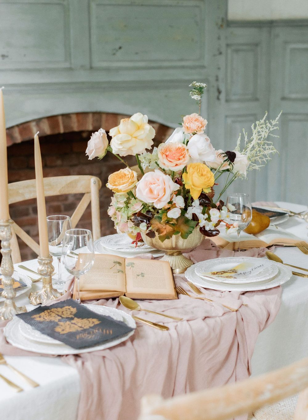 Elegant wedding table setting with blush linens, antique books, and peach and cream floral centerpiece.
