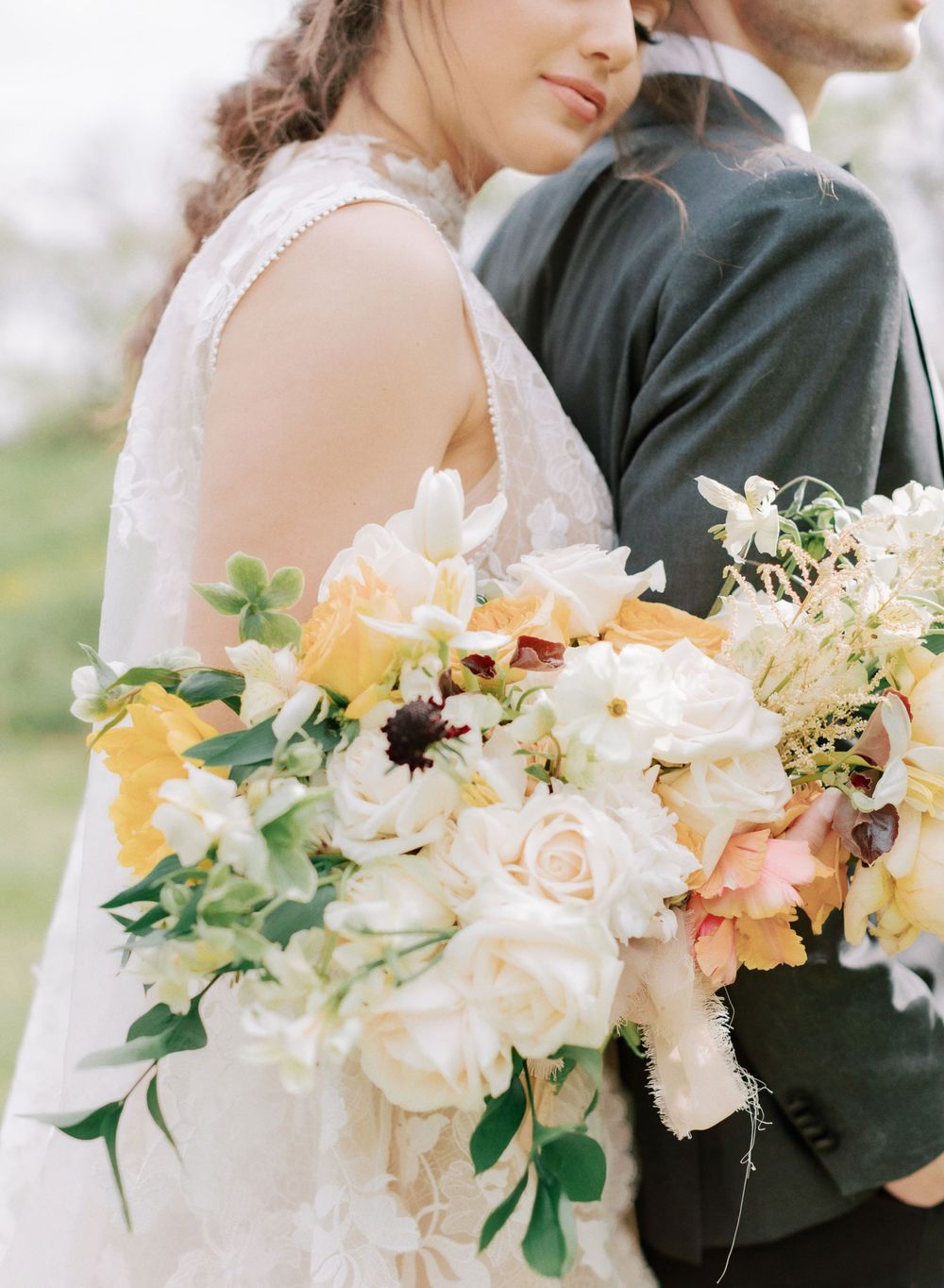 A wedding bouquet with white, peach and yellow flowers against a white lace dress.