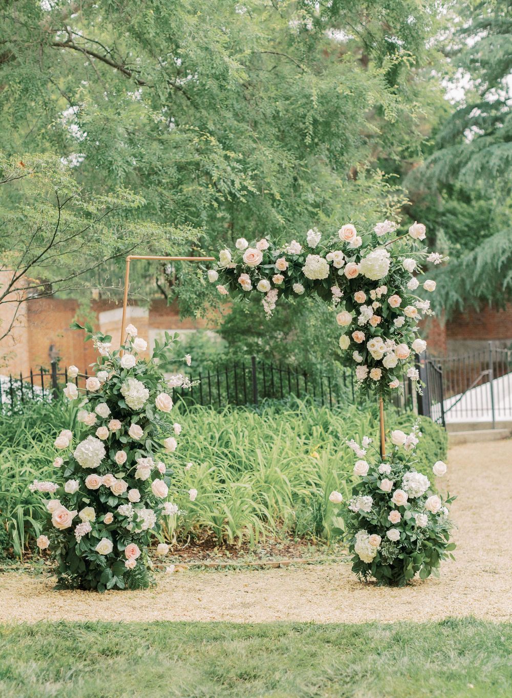 A romantic floral arch with pink and white roses creates an enchanting garden wedding ceremony backdrop.