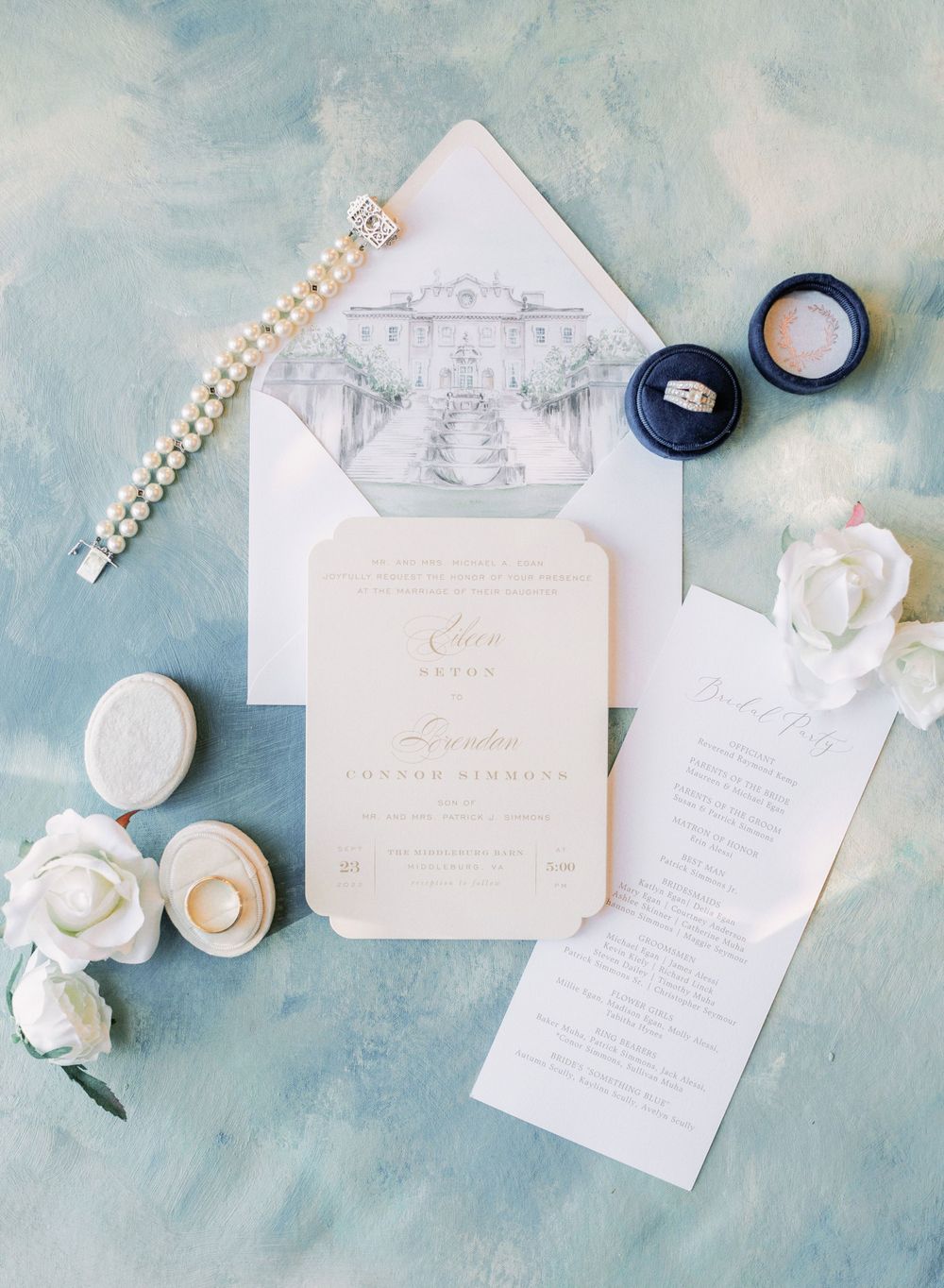Wedding invitation suite with pearl bracelet and white roses on light blue background.