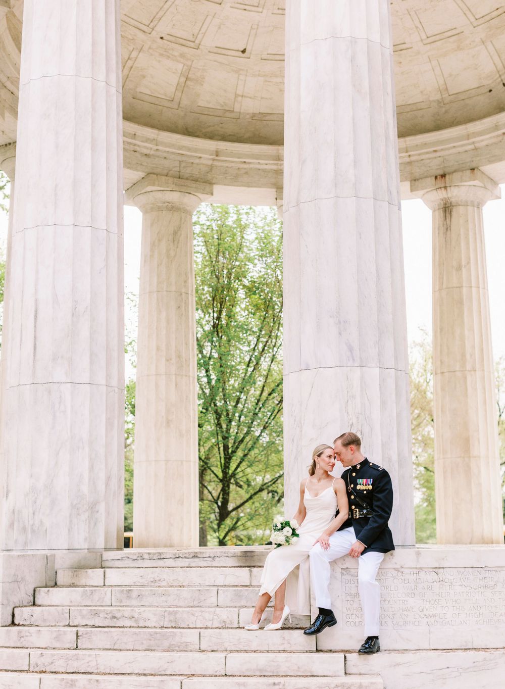 Wedding portrait at a classic marble columned memorial with steps and green trees.