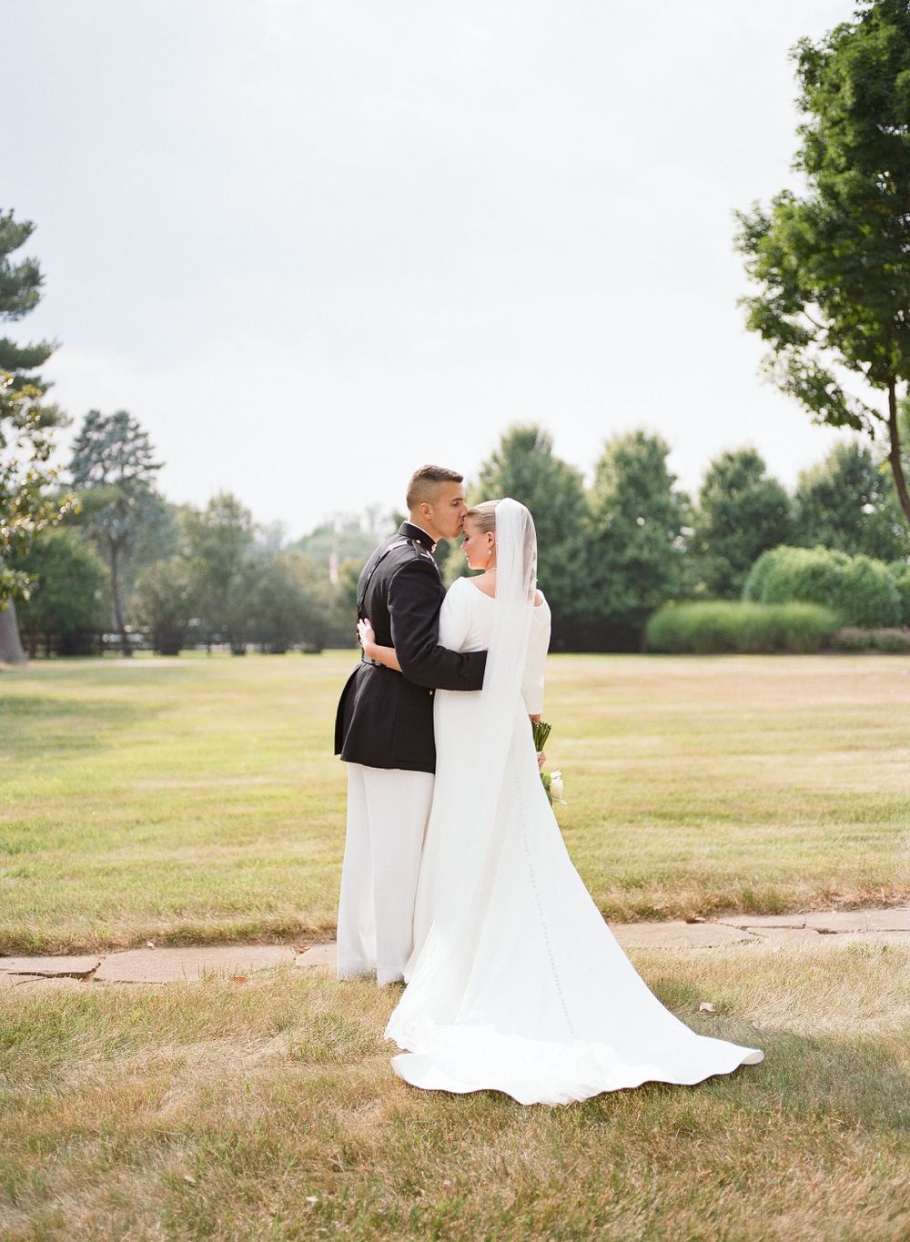 Elegant wedding couple poses in a serene outdoor field with trees in the background.