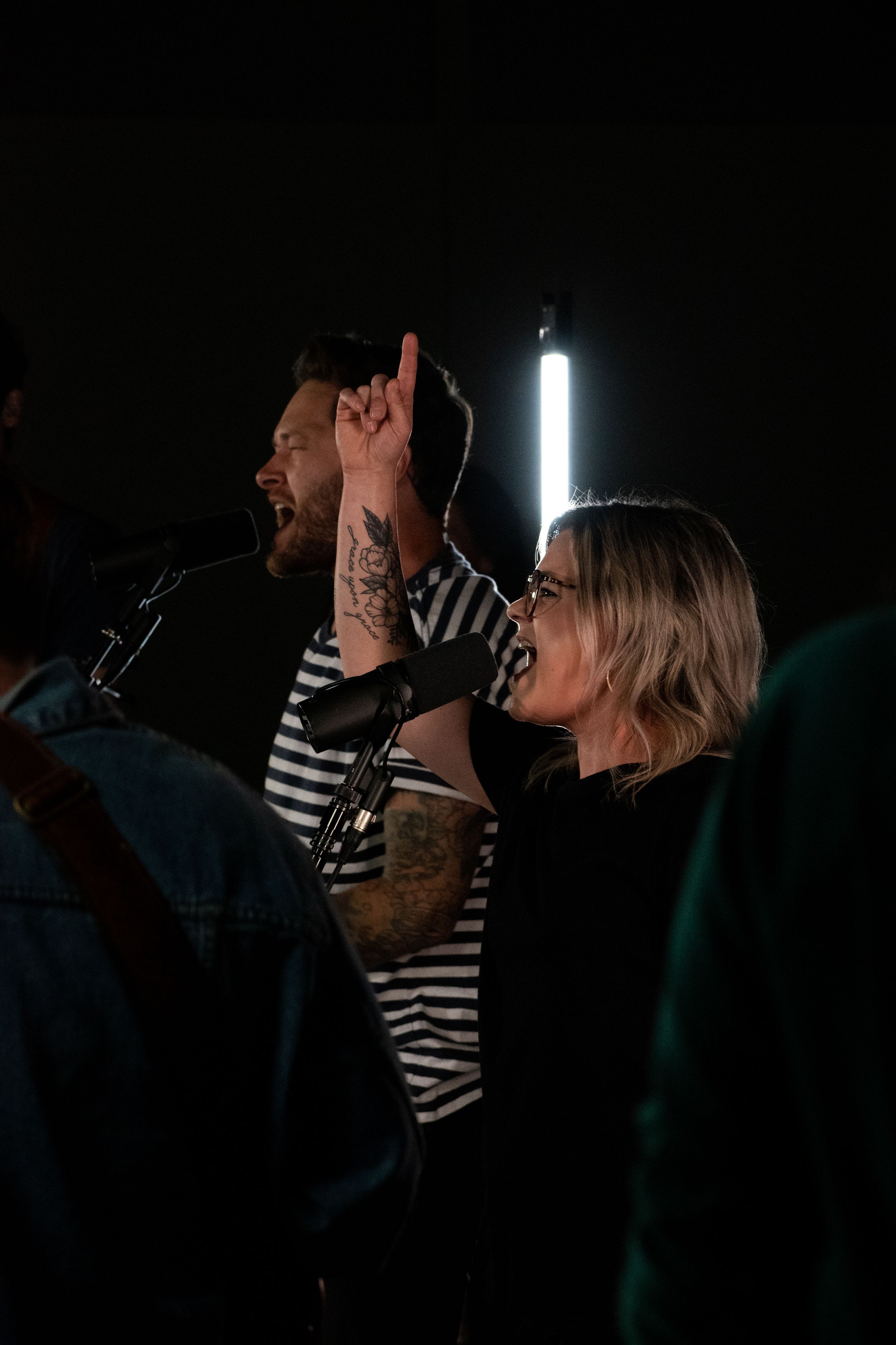 Man with tattoos and woman in striped shirts singing passionately at a live music performance.