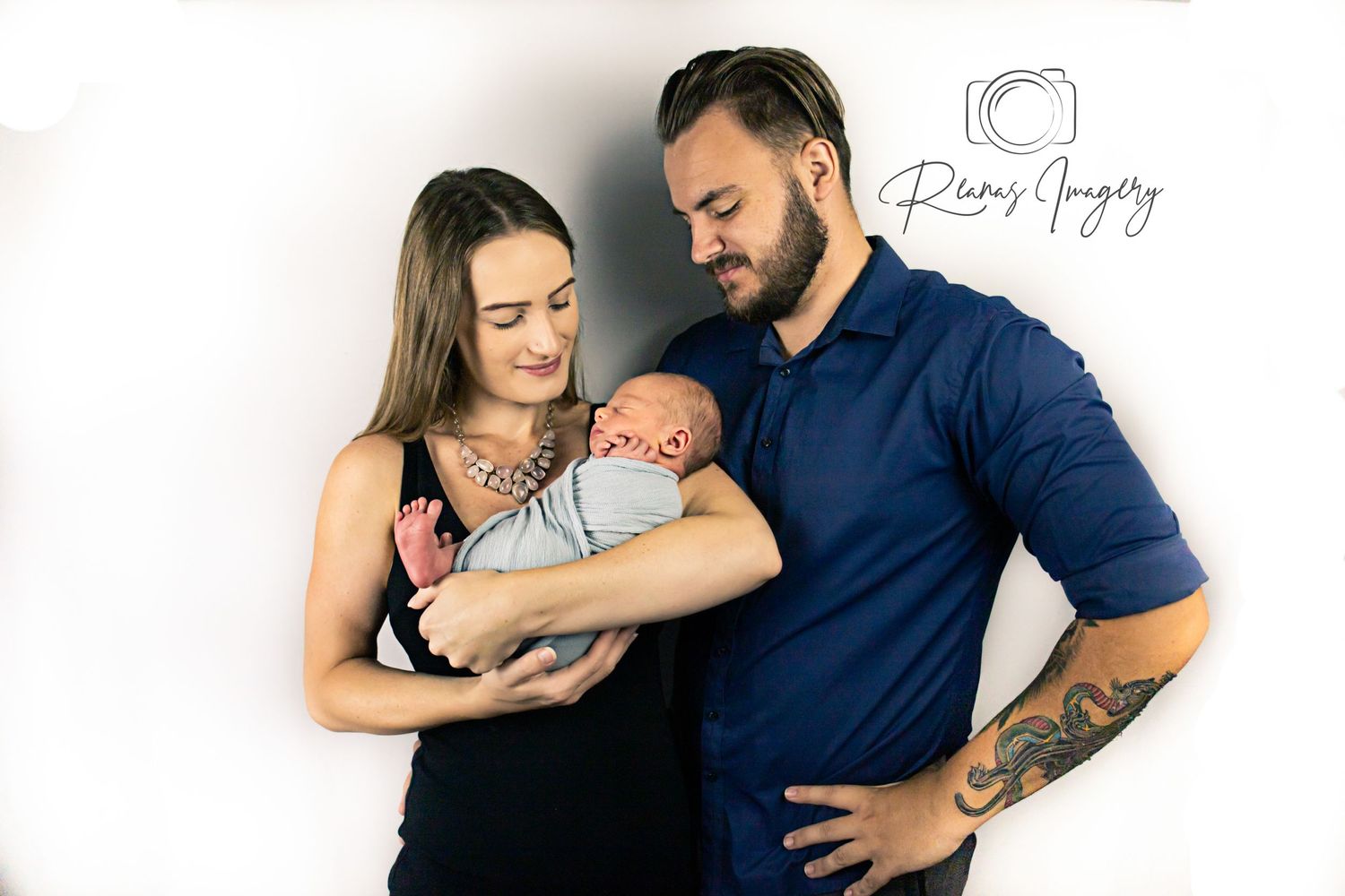 New parents lovingly hold their newborn baby in a professional studio portrait.