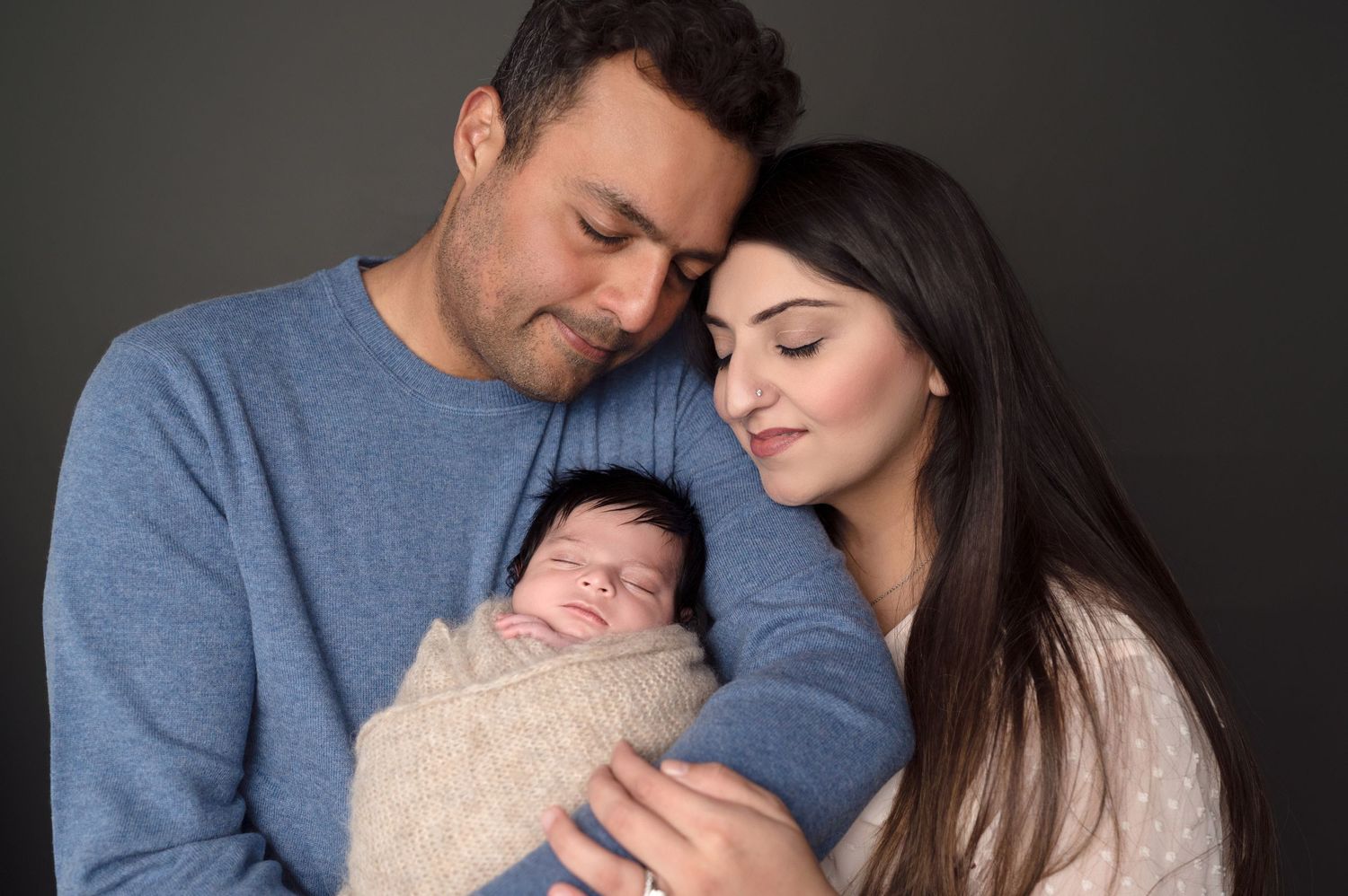 Intimate lifestyle portrait of parents bonding with their newborn in dark tones.