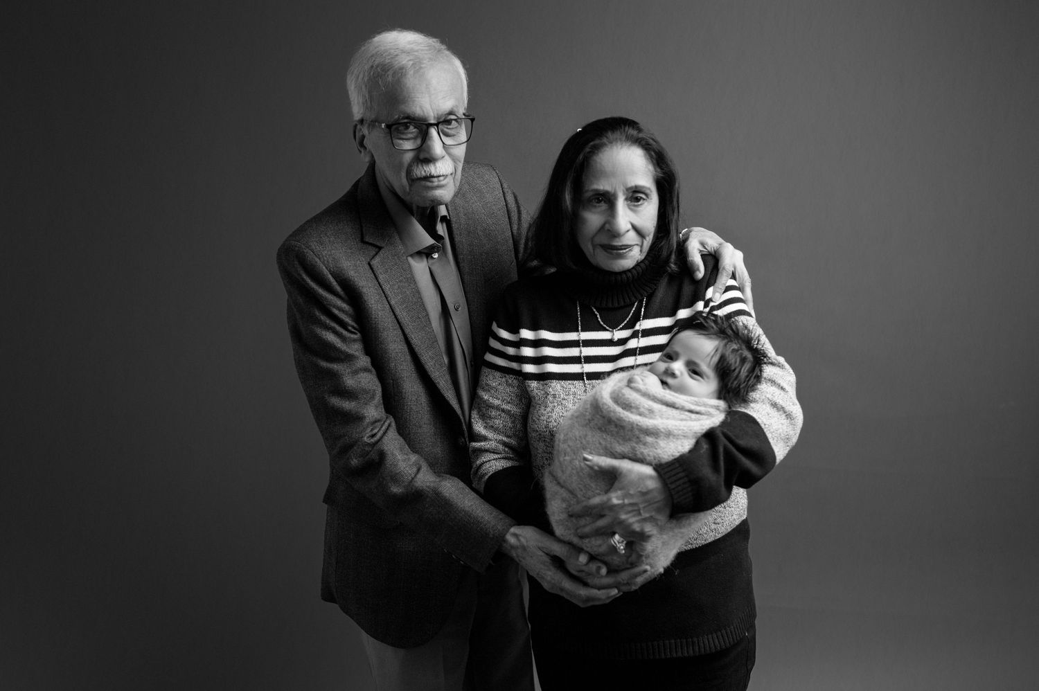 Studio portrait capturing intimate family moment with newborn in dramatic lighting.