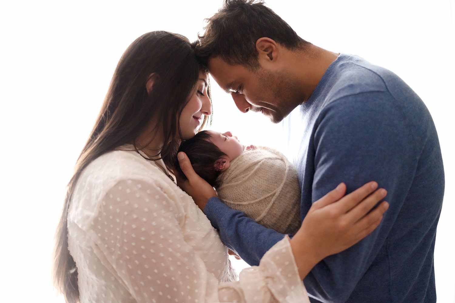 Tender family moment with parents embracing swaddled newborn between them.