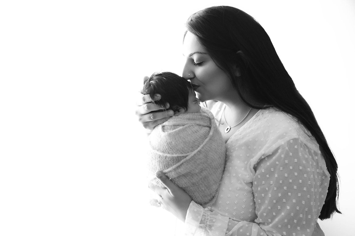 Mother with long dark hair holding swaddled newborn in tender black and white portrait.