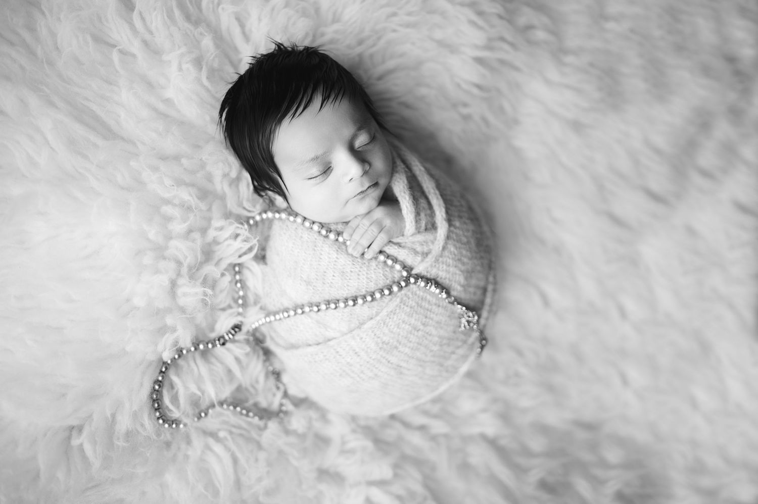 Peaceful sleeping newborn wrapped in white swaddling blanket on soft textured background.