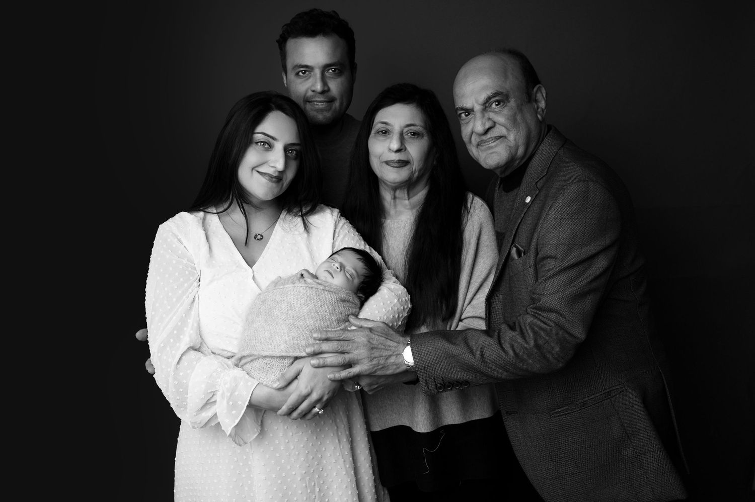 Studio portrait session showing a tender family moment with an infant in black and white.