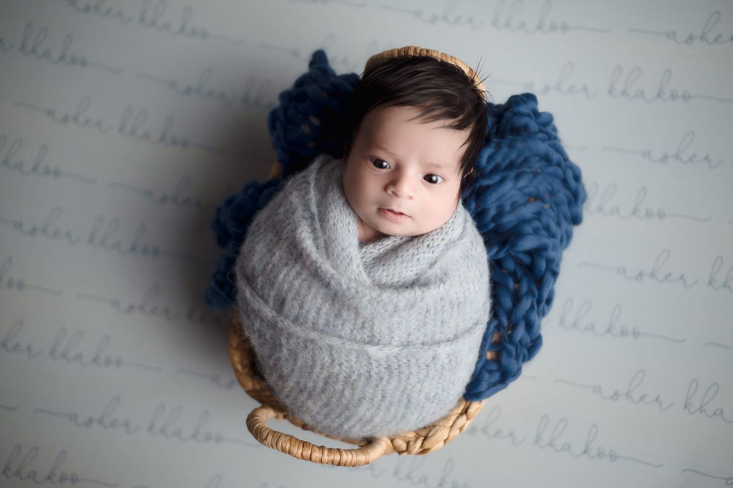 Newborn baby wrapped in gray blanket with blue accent in studio setting.