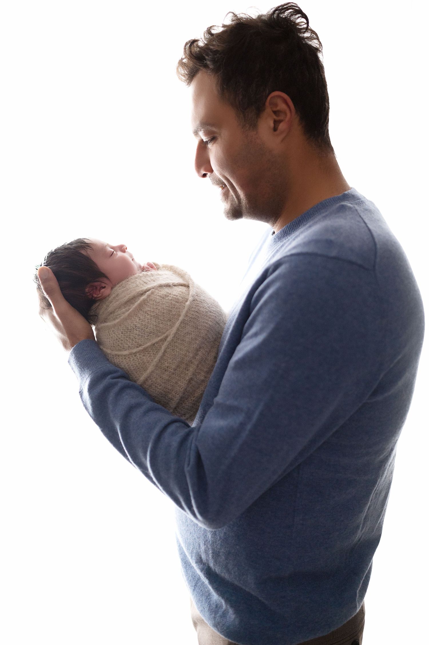Parent in blue sweater holding swaddled newborn against white background.