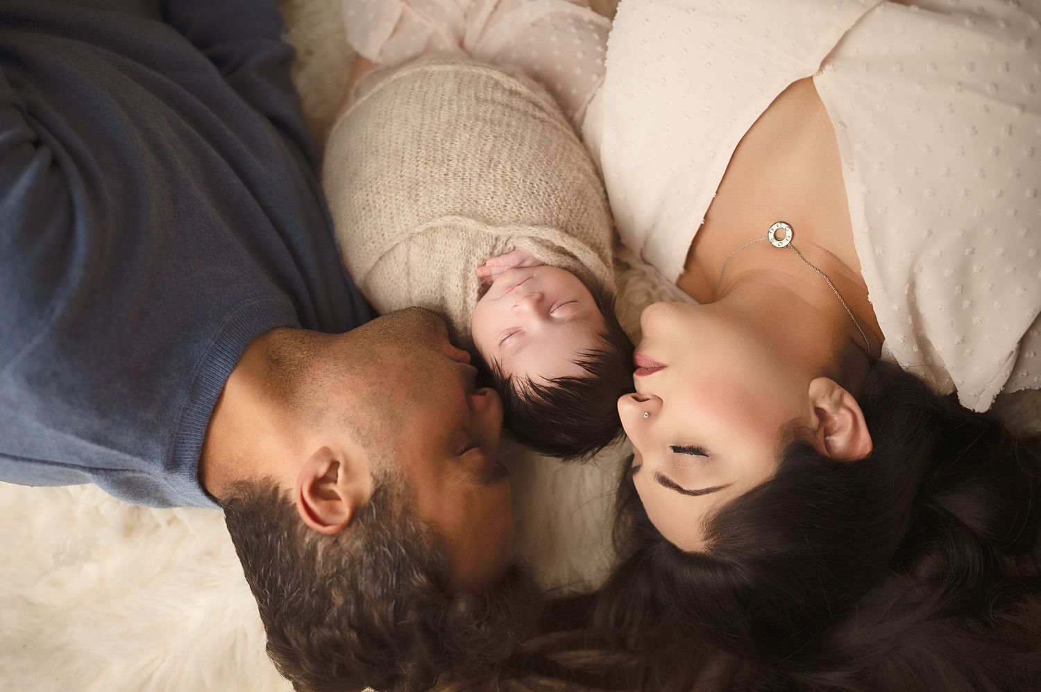 Intimate family portrait with newborn from overhead perspective on cream background.