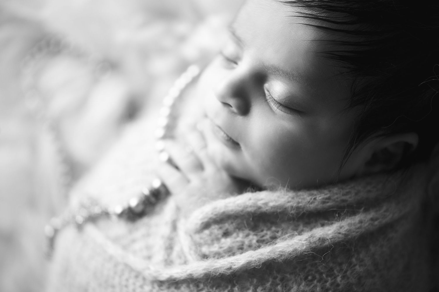 Black and white close-up portrait of sleeping newborn wrapped in cozy blanket.