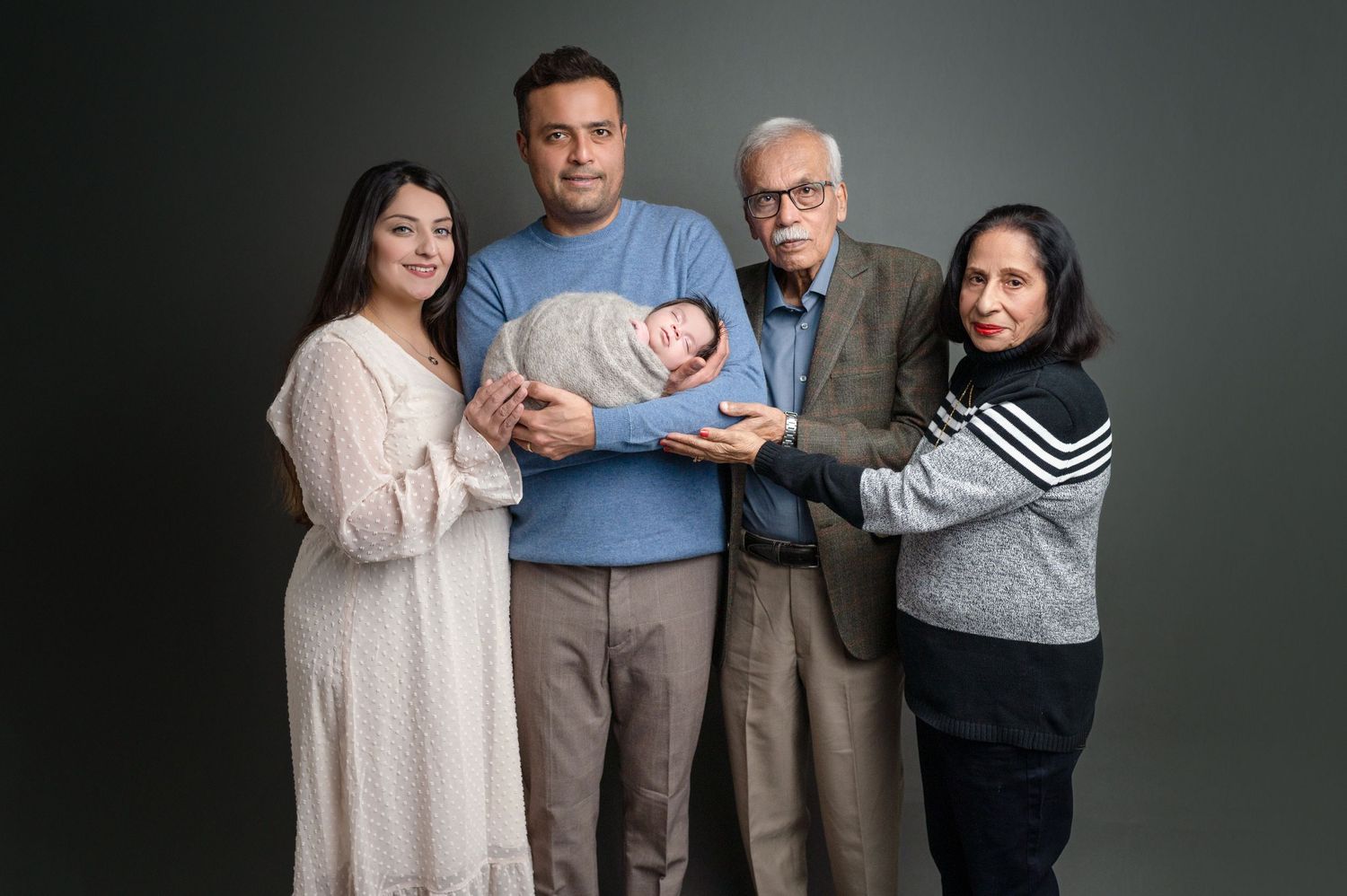 Professional studio portrait of extended family members gathered around a newborn baby.