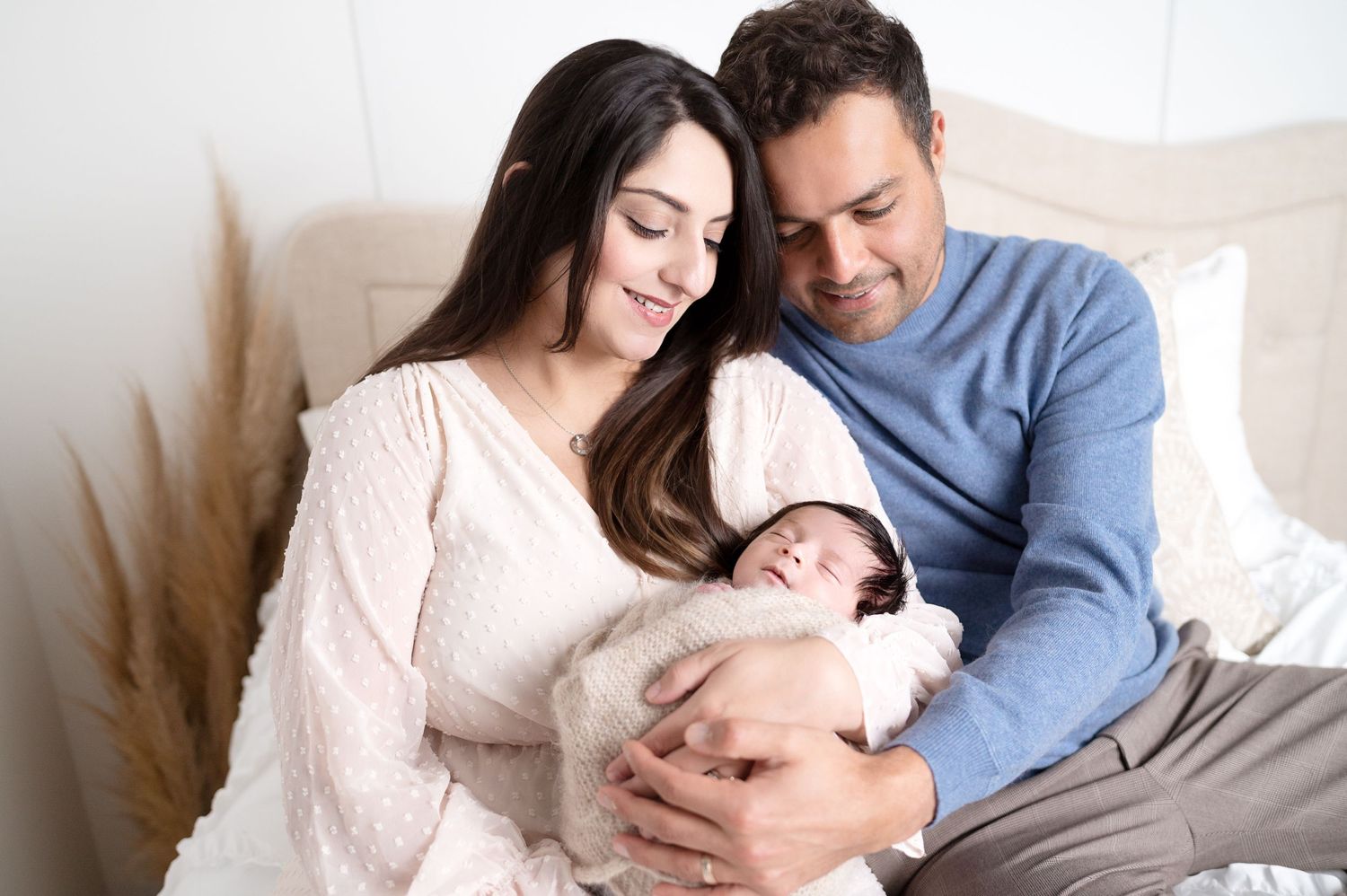 Bright and airy family portrait session with parents cuddling their newborn on white bedding.