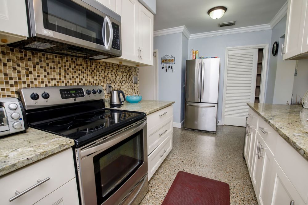 White kitchen with granite countertops features modern appliances and recessed lighting.