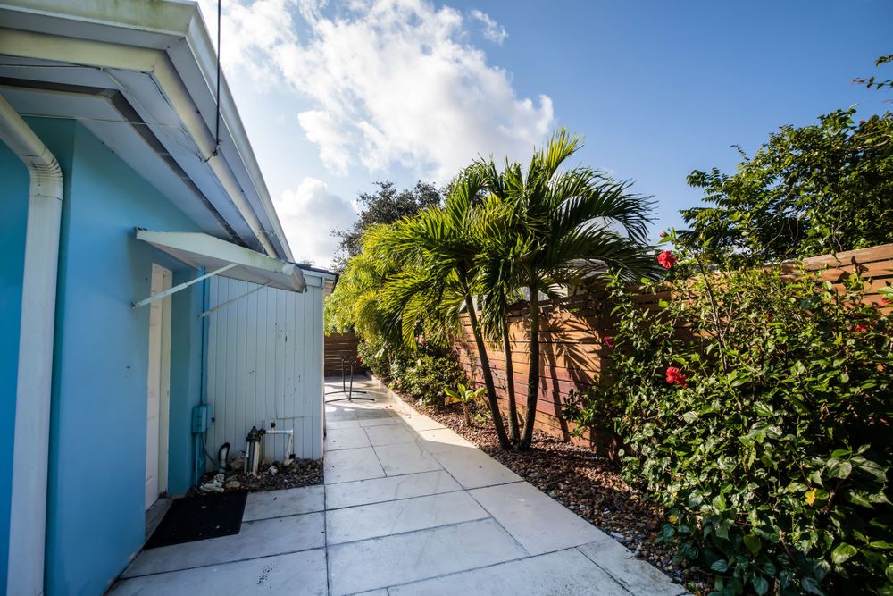Side view of light blue house with concrete walkway and tropical garden landscaping.