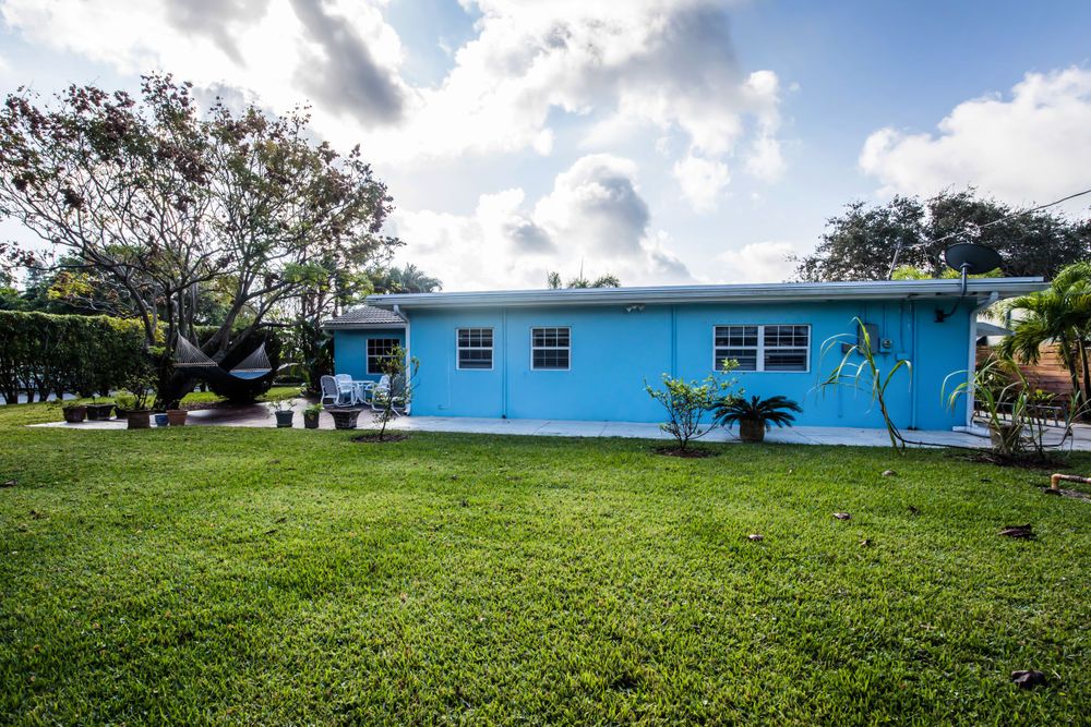 Panoramic view of a blue residential house with manicured lawn and tropical landscaping.