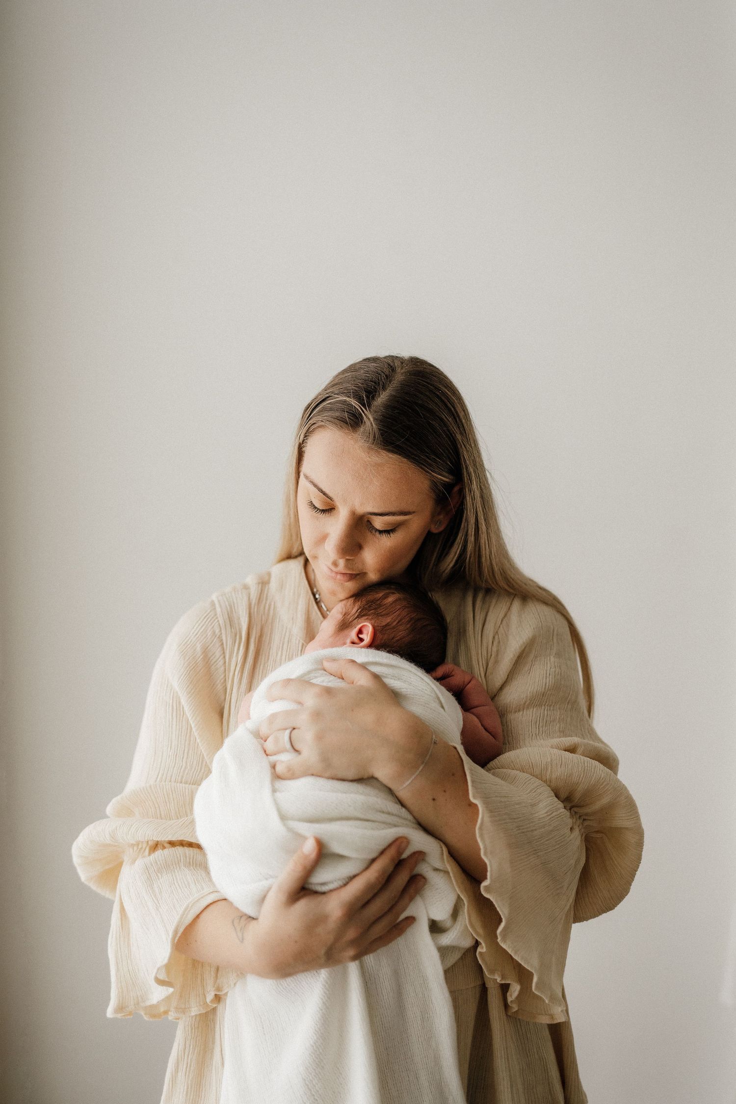 Parent in beige sweater holding and bonding with baby against white backdrop.
