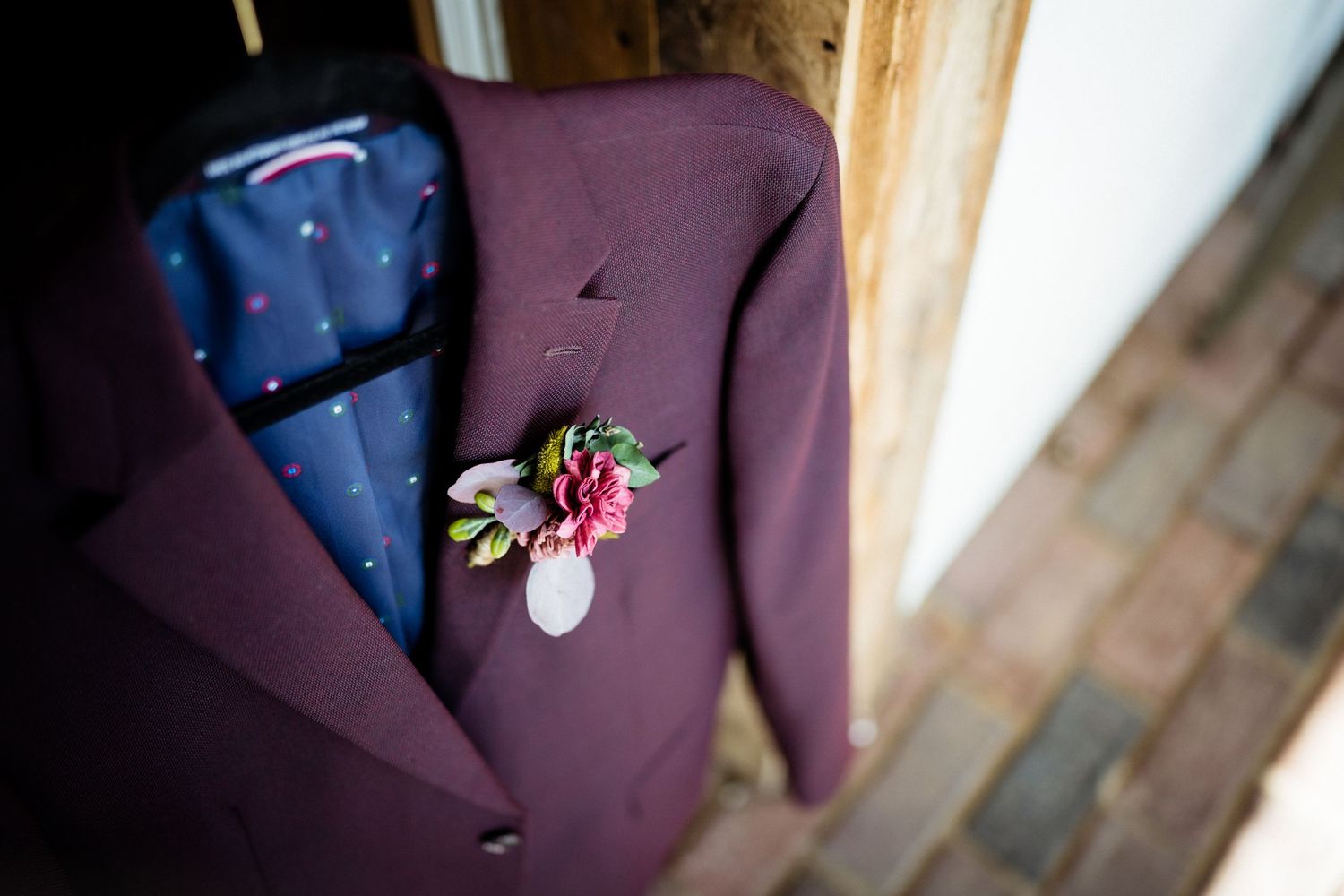 A purple suit jacket with delicate pink floral boutonniere displayed against wooden background.