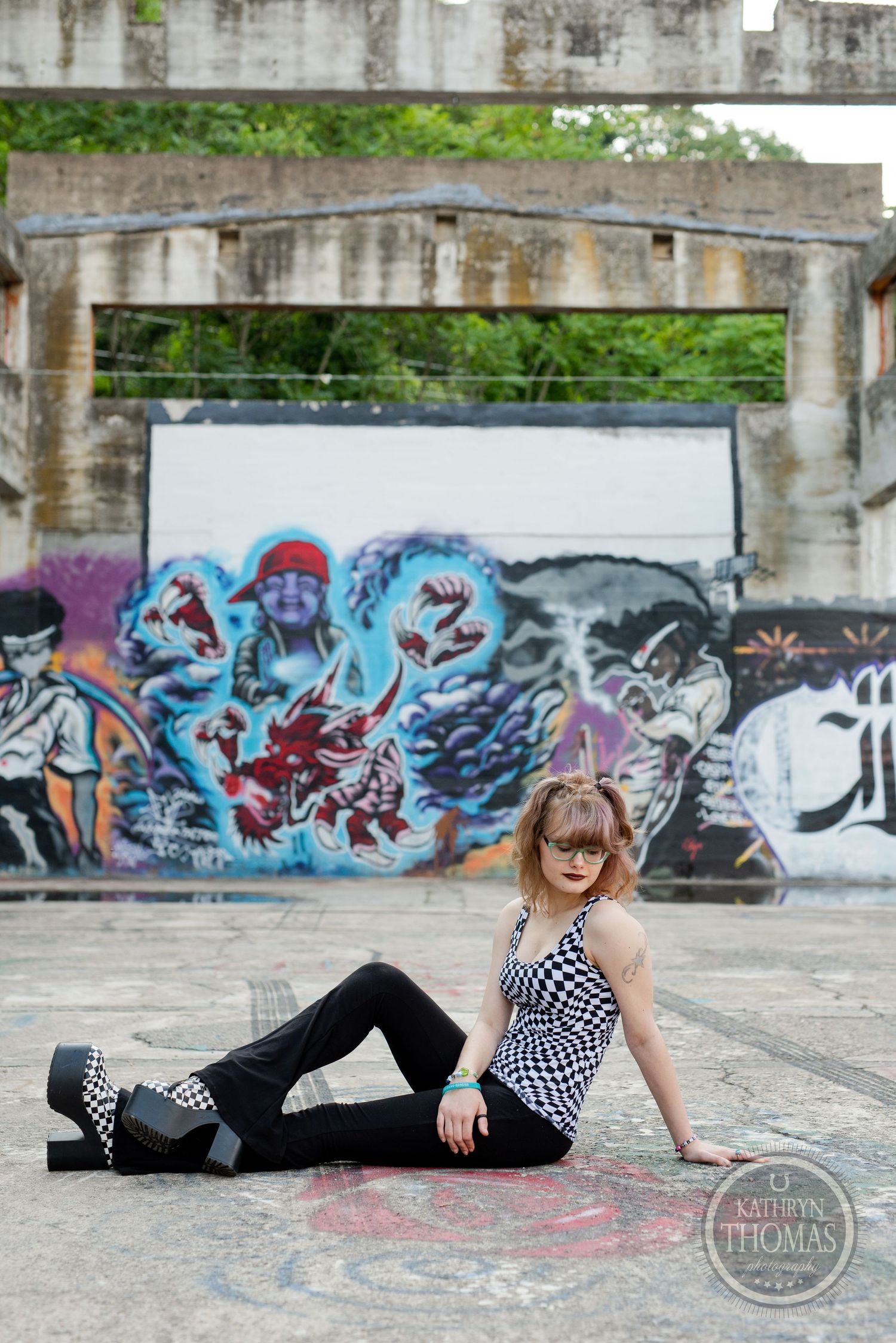 A person in checkered top and flared pants reclines against urban graffiti wall.