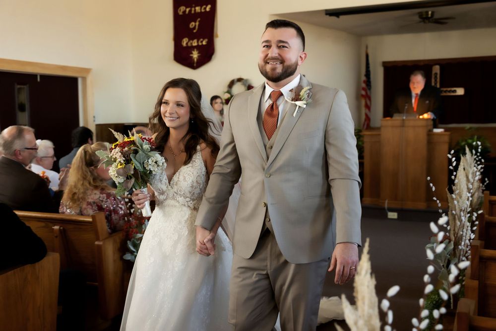 A joyful couple exits the church ceremony while guests look on from wooden pews.