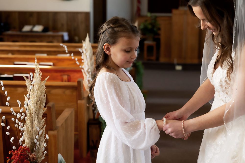 A tender moment between a bride and young attendant in white dress inside a church sanctuary.