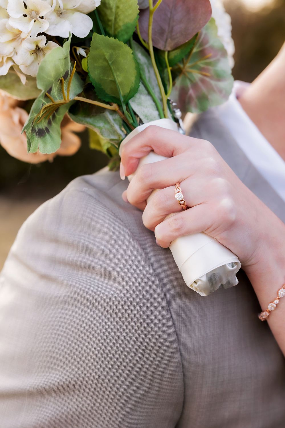 Close-up of hands holding a wedding bouquet showing an engagement ring and delicate bracelet.