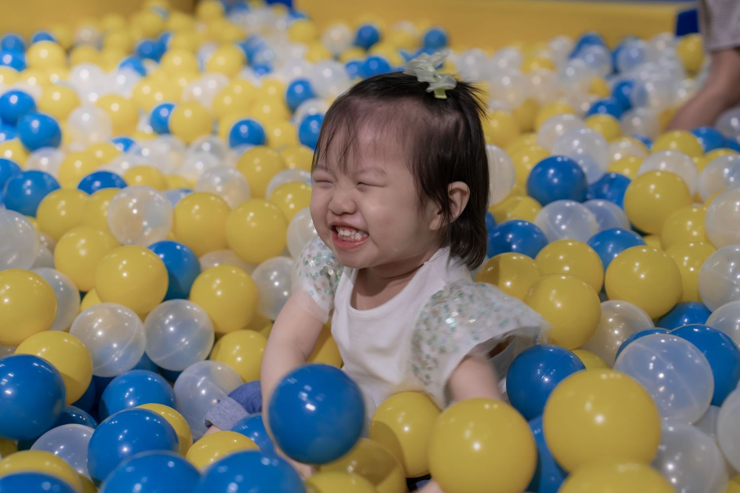 Child playing in a ball pit filled with blue, yellow and white balls while laughing joyfully.