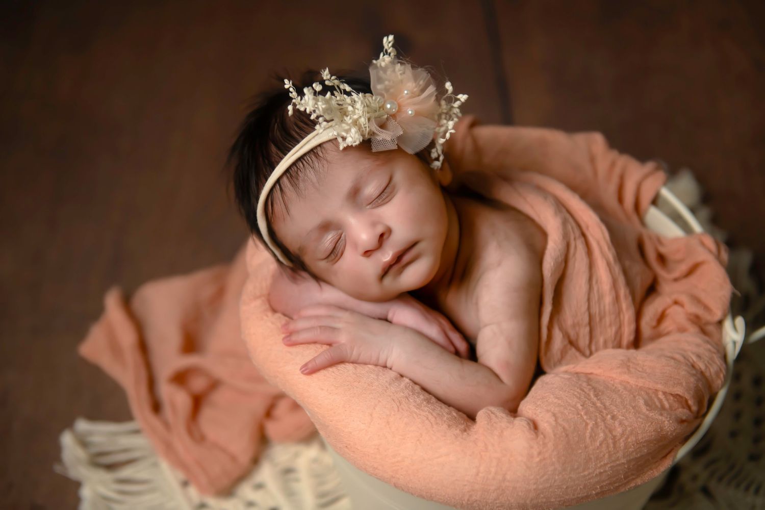 Delicate newborn photography featuring sleeping baby on peach backdrop with soft lighting.