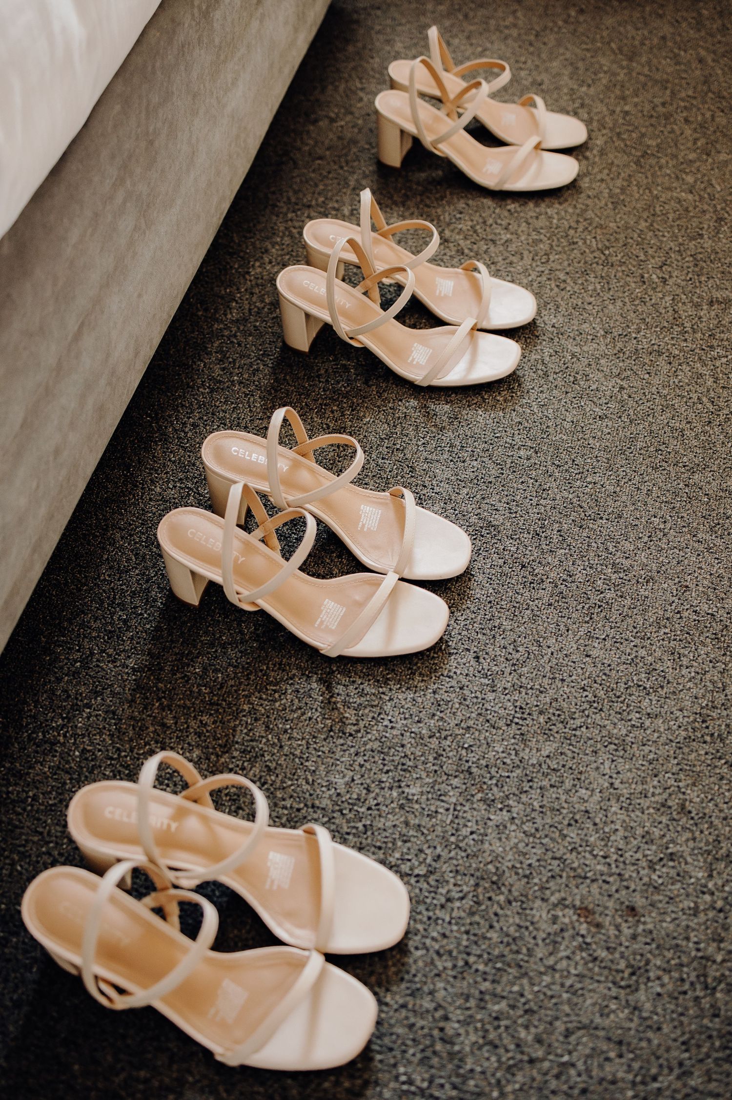 Four pairs of beige slingback sandals with small block heels lined up neatly on a dark carpet floor.