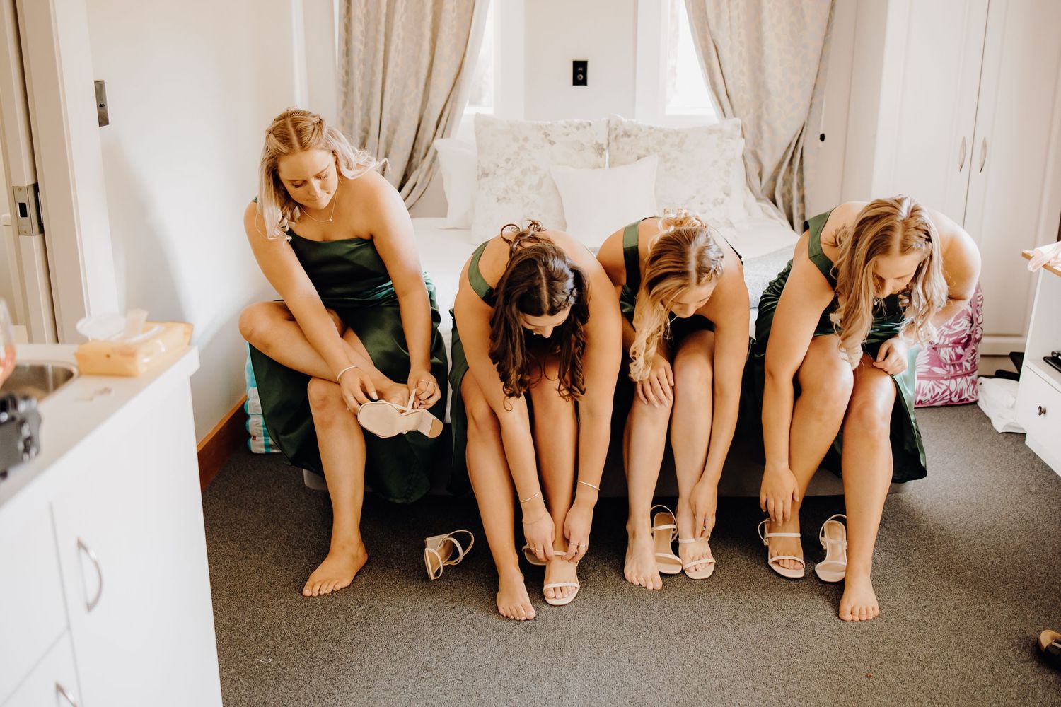 Four people in matching outfits sit in a row while putting on shoes in a bright white room.
